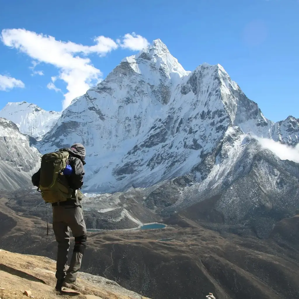 A hiker standing on a rocky terrain with snow-capped mountains in the background at Everest Base Camp.